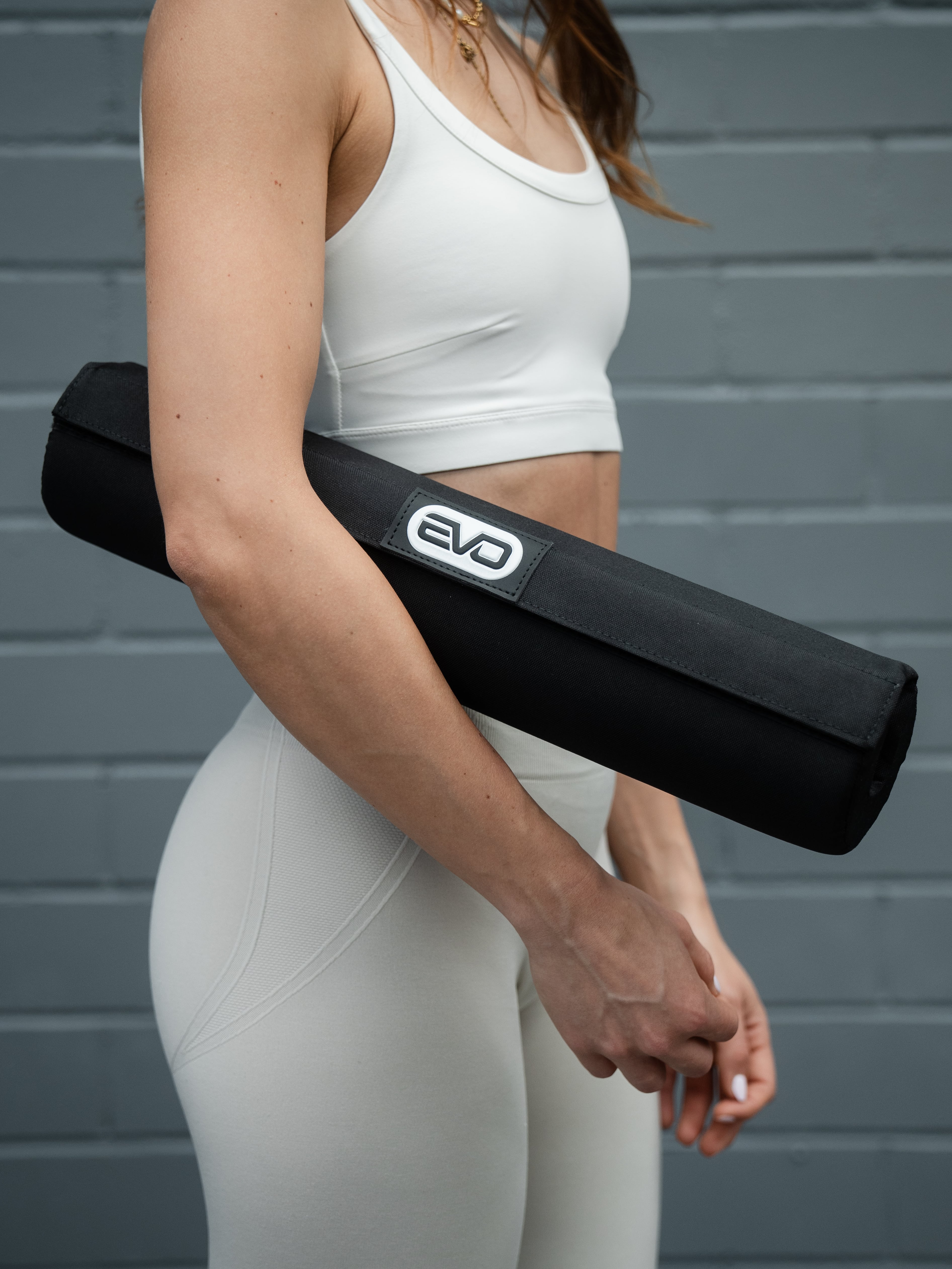 Mädchen in weißer Kleidung hält ein schwarzes EVO Barbell Pad in ihrer rechten Hand.